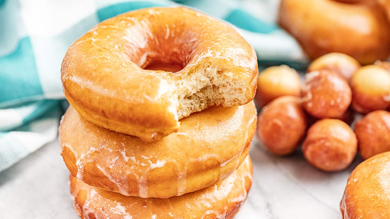 A stack of 3 glazed donuts with a bite taken out of the top donut