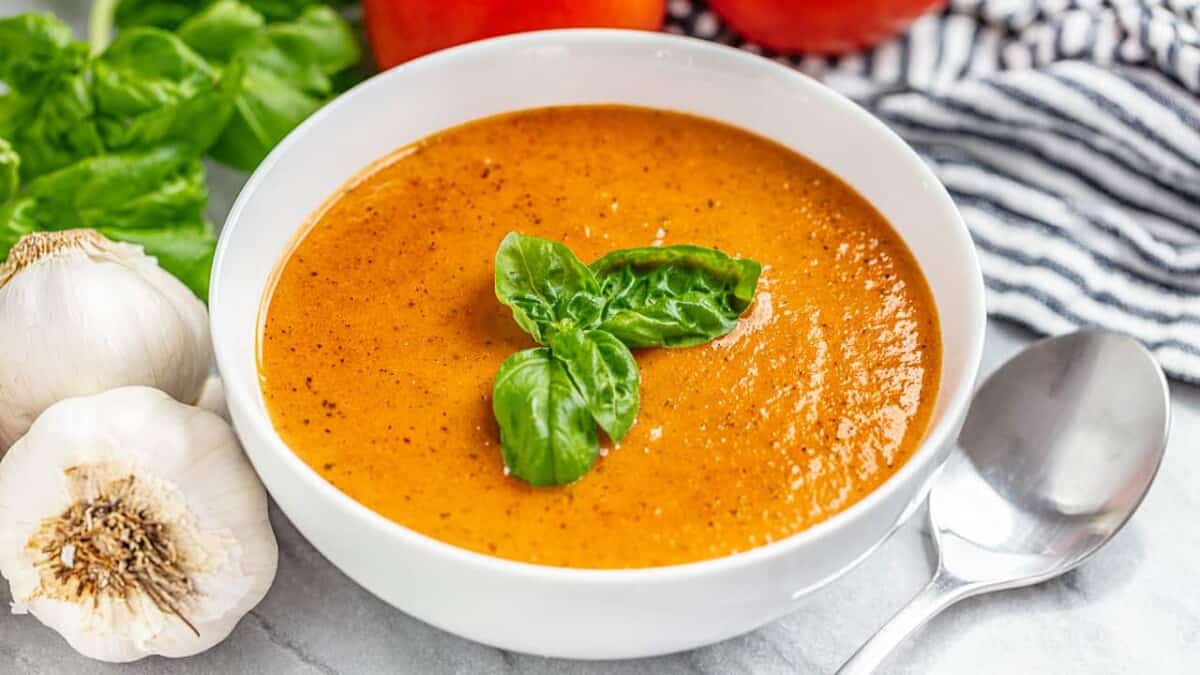 A bowl of tomato basil soup with fresh basil on top and a spoon next to the bowl