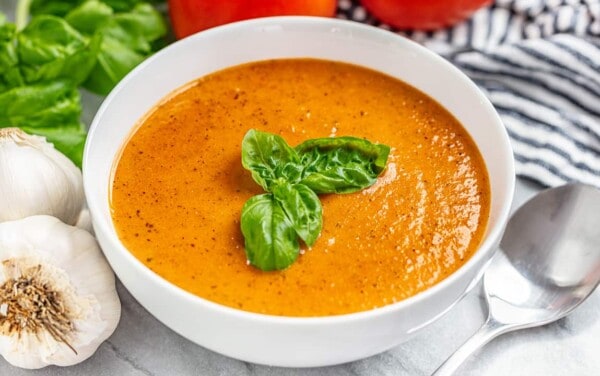 A bowl of tomato basil soup with fresh basil on top and a spoon next to the bowl
