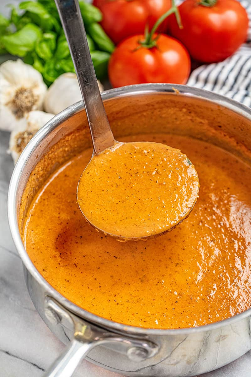 a saucepan filled with tomato basil soup and a ladle hovering over, filled with soup