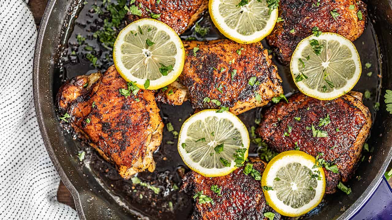 Chicken thighs in a skillet with parsley and lemon slices