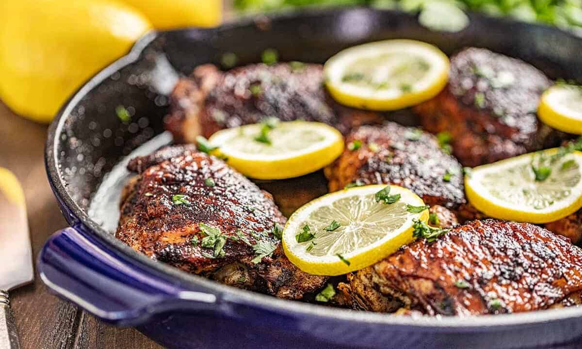 Close up view of cooked chicken thighs in a skillet with lemon slices on top