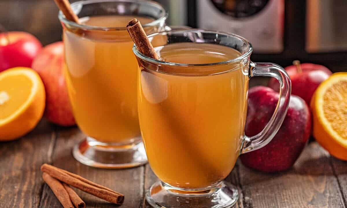 2 glass mugs full of apple cider with a cinnamon stick in each