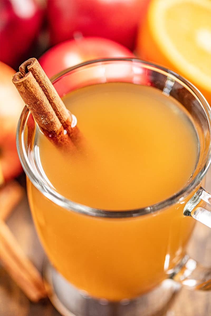 A glass mug full of apple cider with a cinnamon stick