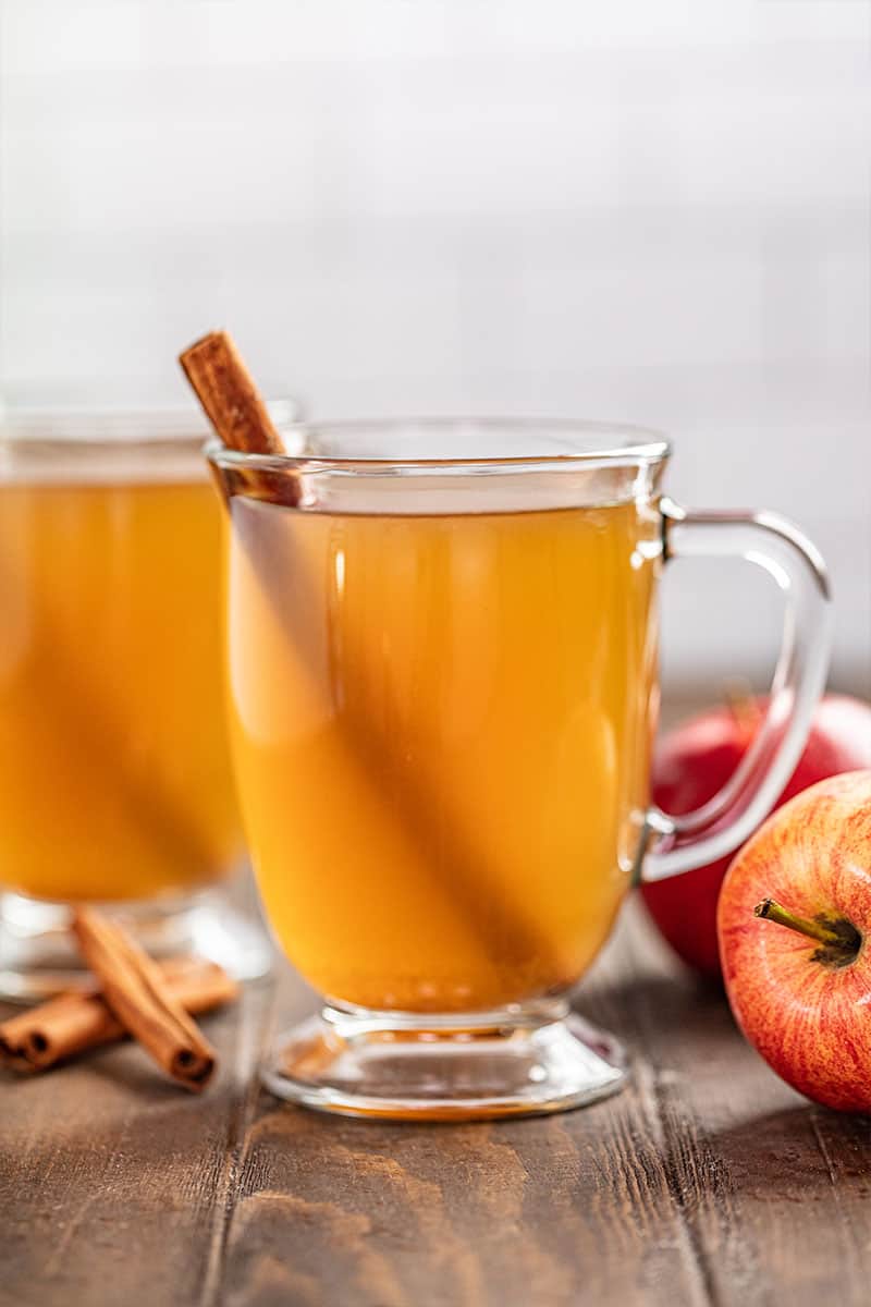 Glasses of apple cider with a cinnamon stick and fresh apples nearby