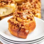 A maple pecan sticky bun on a stack of white plates.