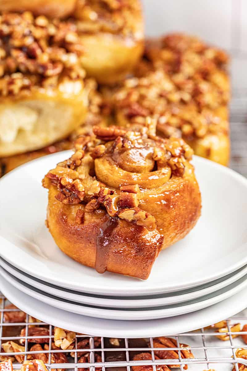 A maple pecan sticky bun on a stack of white plates.