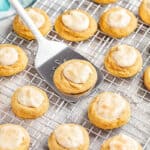 A spatula scooping up a Pumpkin Cheesecake Thumbprint cookies off a wire cooling rack.