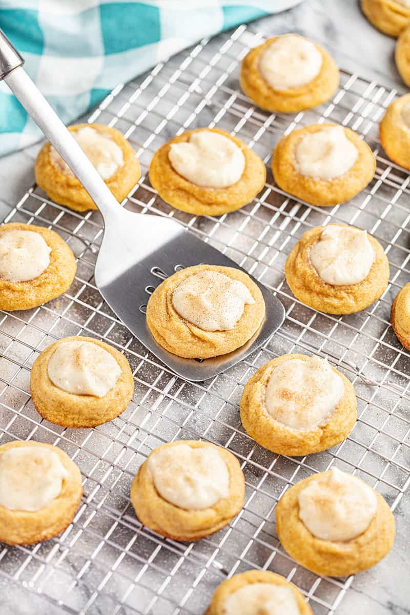 A spatula scooping up a Pumpkin Cheesecake Thumbprint cookies off a wire cooling rack.
