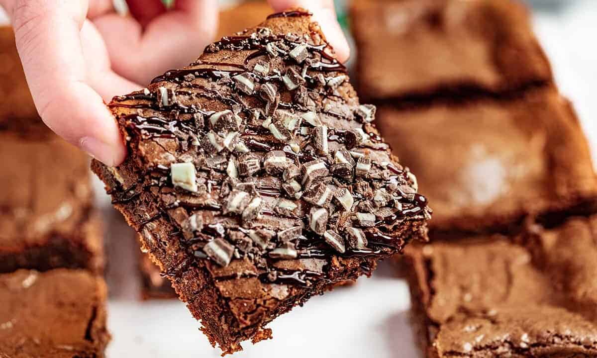 Close up view of someone's hand holding a brownie with Andes mints crushed on top.