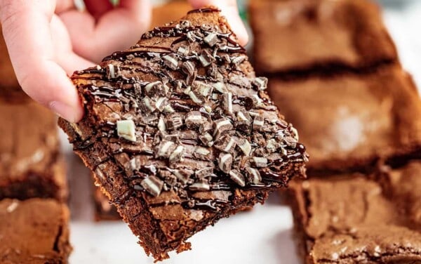 Close up view of someone's hand holding a brownie with Andes mints crushed on top.