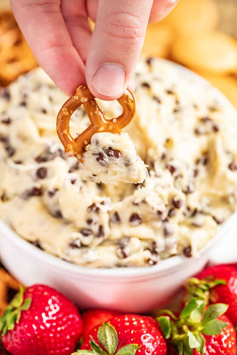 Someone dipping a pretzel into chocolate chip cookie dough dip.