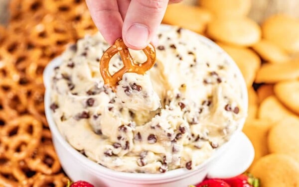 A pretzel being dipped into a bowl of chocolate chip cookie dough dip.