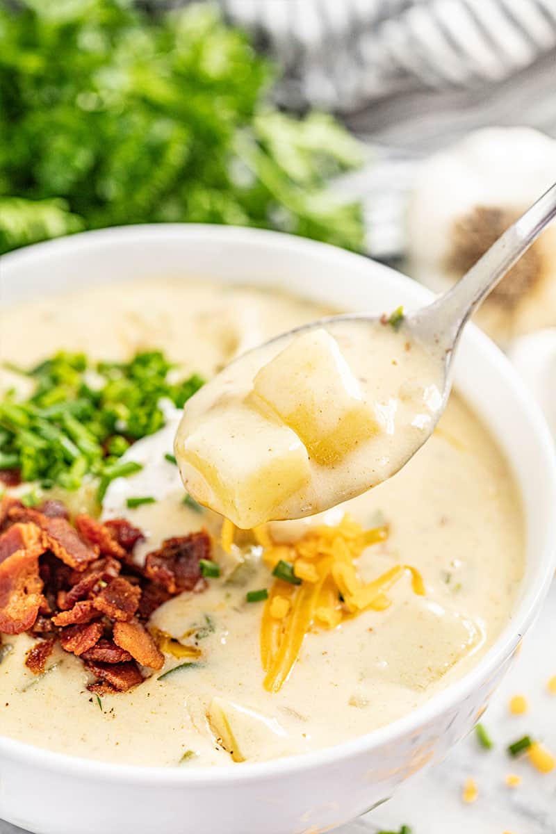 A spoon dipping into a bowl of creamy potato soup.