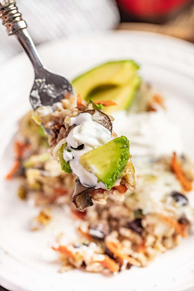 Close up view of a forkful of brown rice and black bean casserole with avocado.