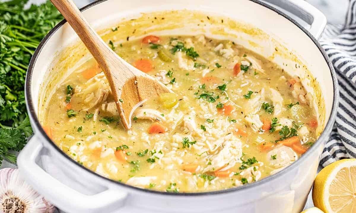 A stock pot full of chicken and rice soup with a wooden spoon inside.