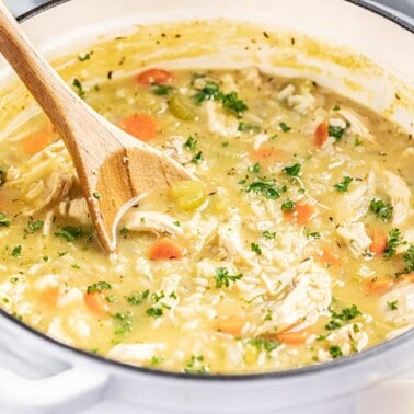 A stock pot full of chicken and rice soup with a wooden spoon inside.
