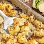 Close up view of a spatula holding up roasted cauliflower from a sheet pan.