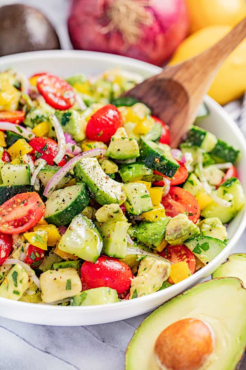 A wooden spoon resting in a bowl of tomato and avocado salad.