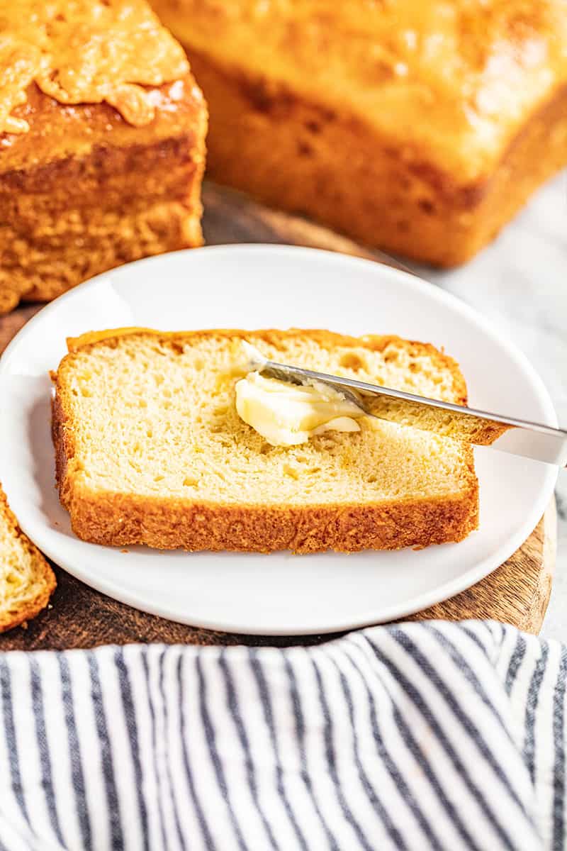 Butter being spread over a slice of cheddar batter bread.