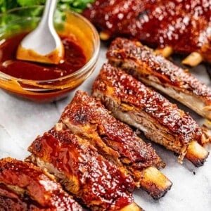 Oven baked ribs with a bowl of sauce on the side.