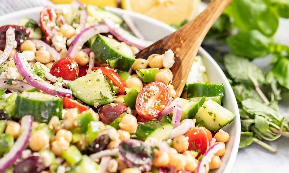 A bowl of mediterranean chickpea salad with a wooden spoon.