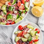 Overhead view of a serving bowl and a side salad plate filled with greek salad.