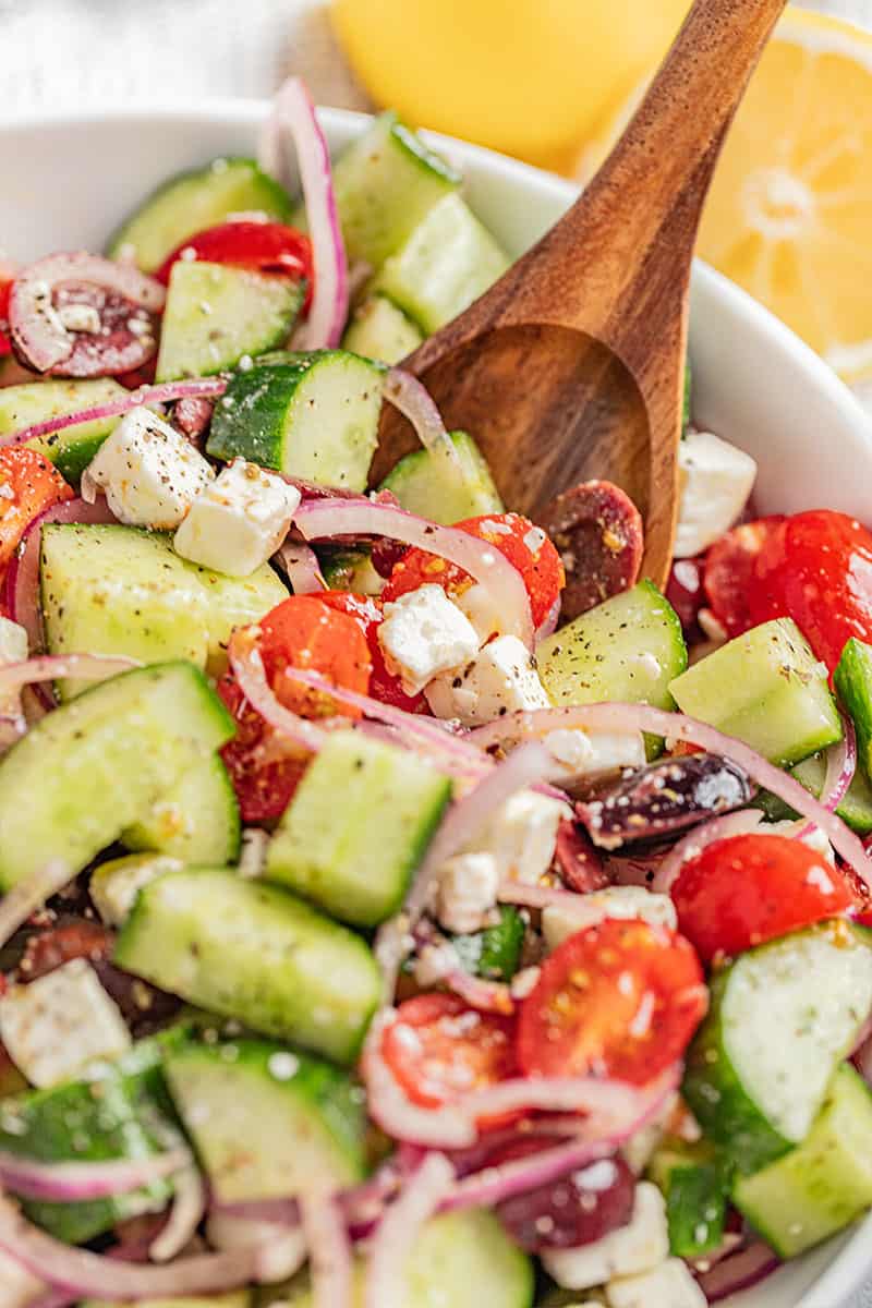 A wooden spoon dipped into a bowl of greek salad.