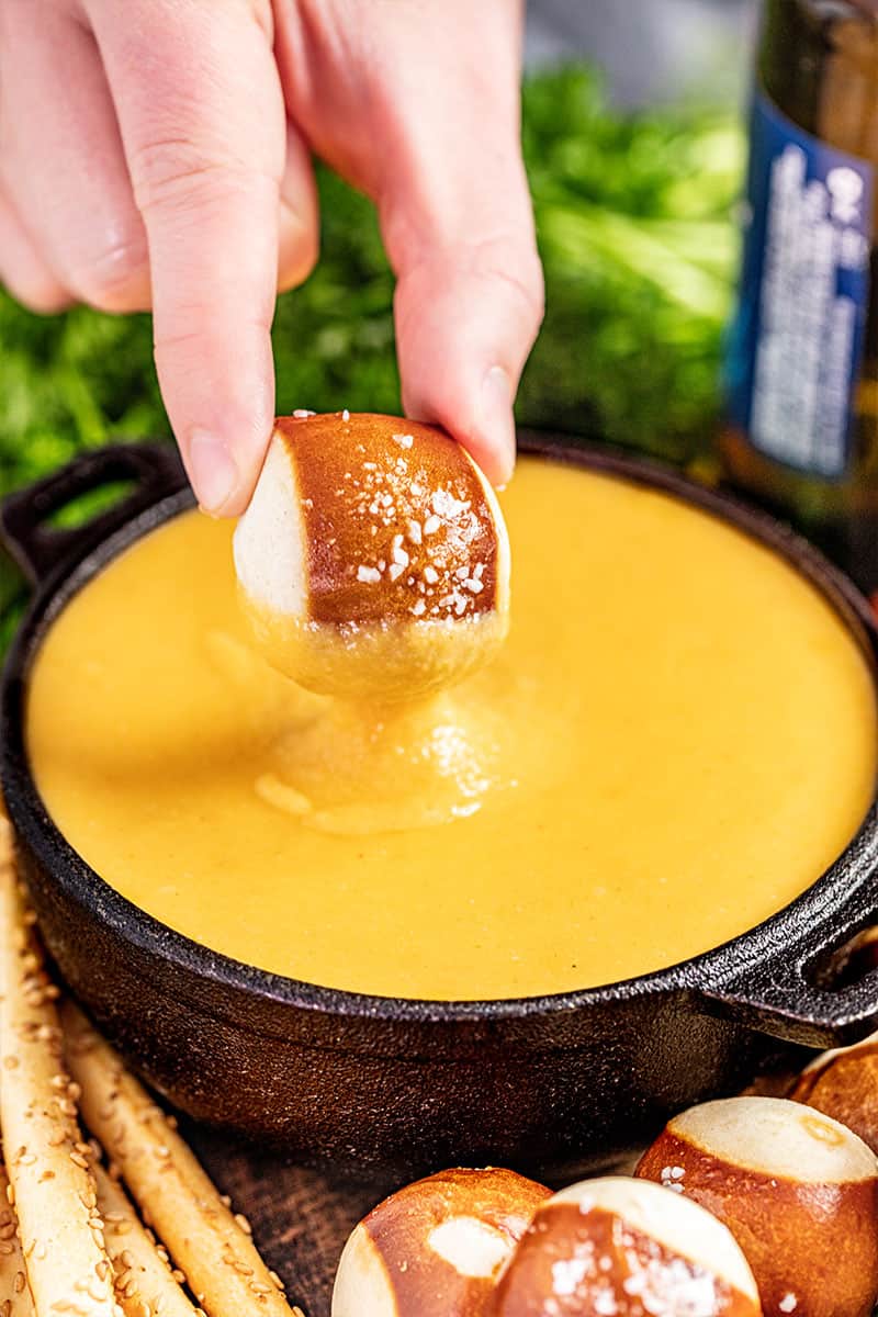 A hand dipping a pretzel bite into a pot of beer cheese dip.
