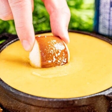 A hand dipping a pretzel bite into beer cheese dip.