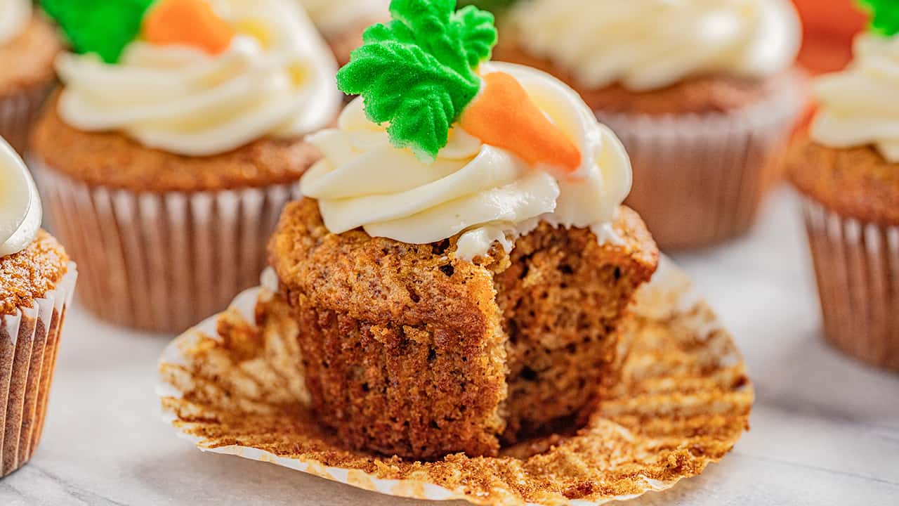 A carrot cake cupcake with the wrapper unwrapped and a bite taken out of it.
