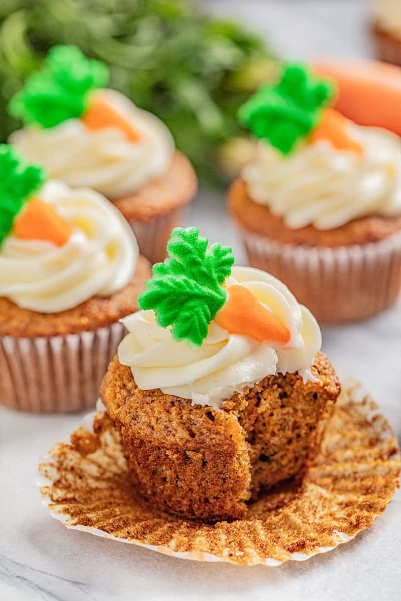 A carrot cake cupcake with cream cheese frosting with a bite taken out.