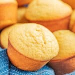 A towel lined basked filled with cornbread muffins.