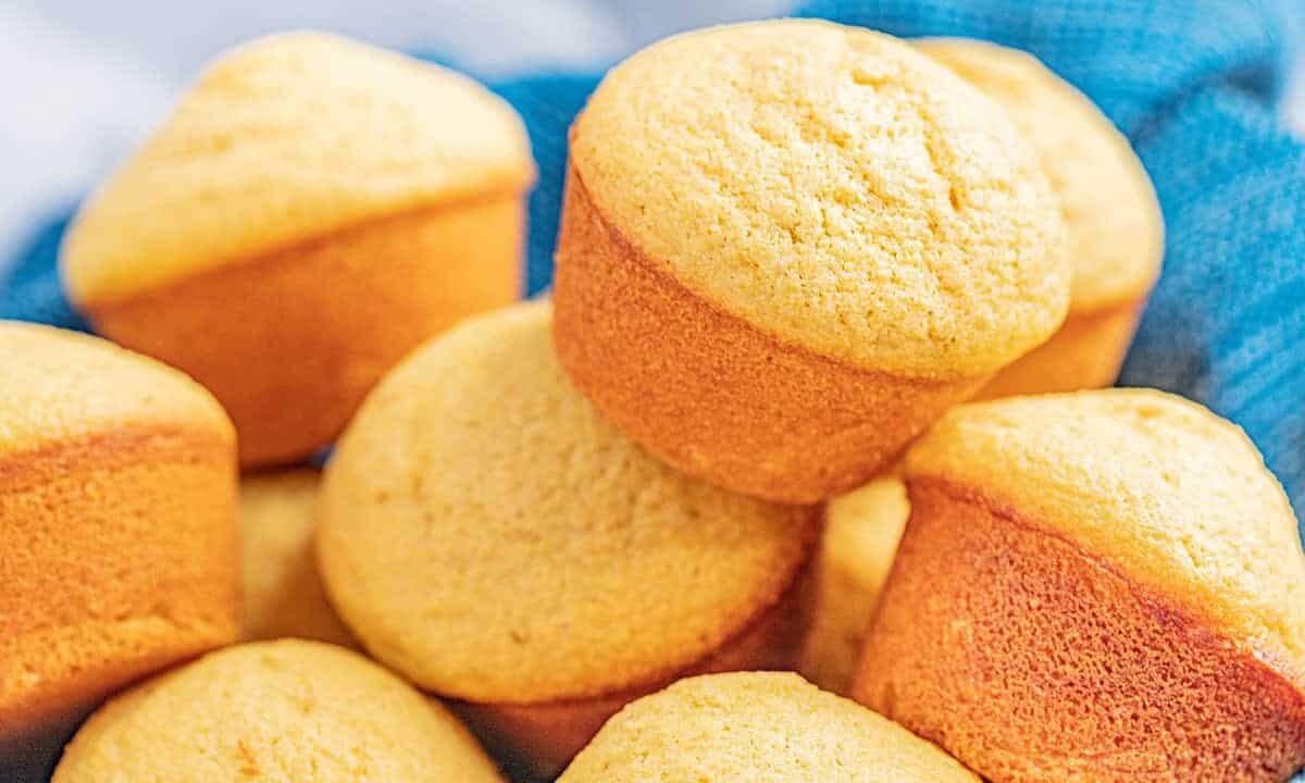 A basket lined with a towel and filled with cornbread muffins.