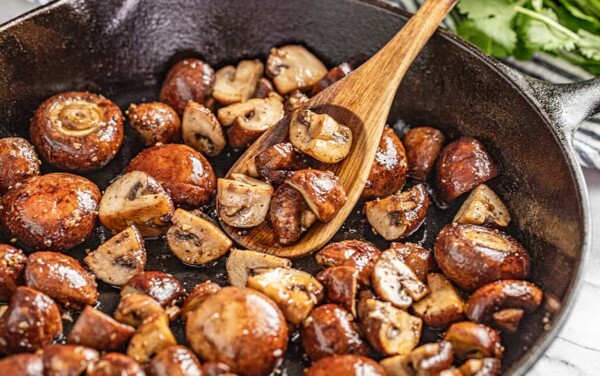 A wooden spoon scooping sautéed mushrooms out of a skillet.