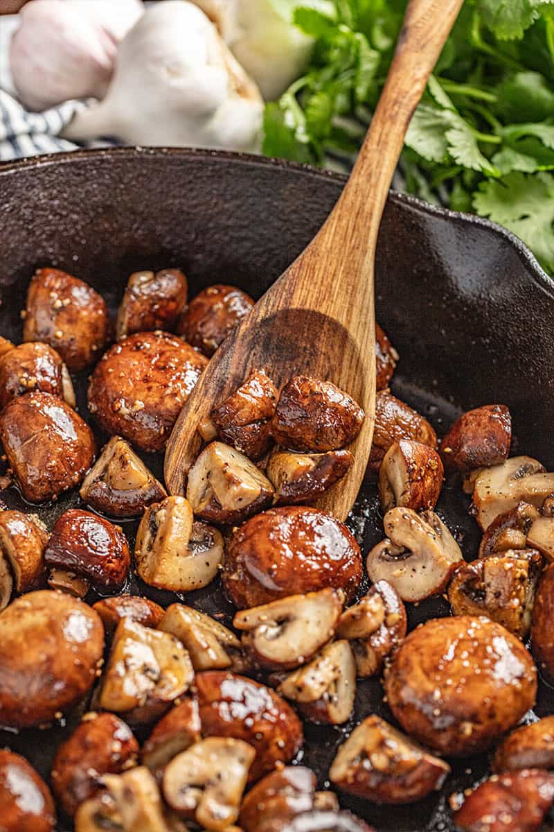 Scooping sautéed mushrooms out of a skillet.
