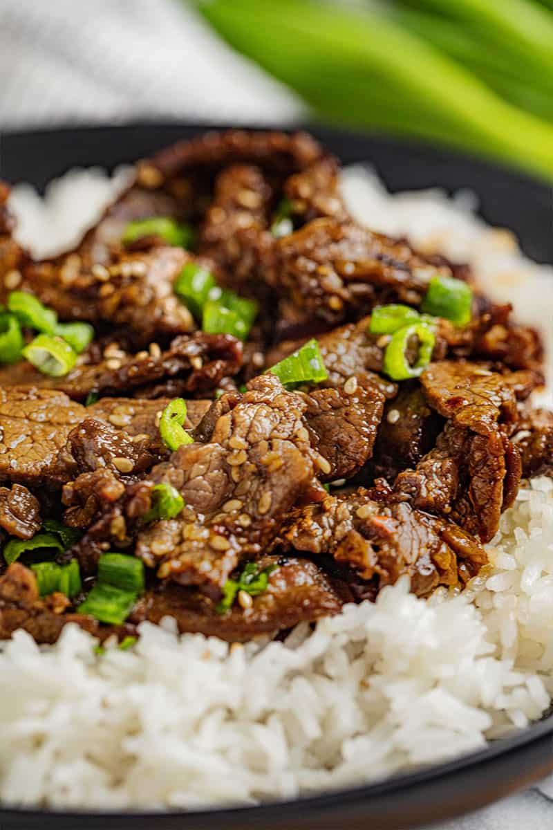 Korean beef bulgogi with chopped green onions on a bed of white rice.