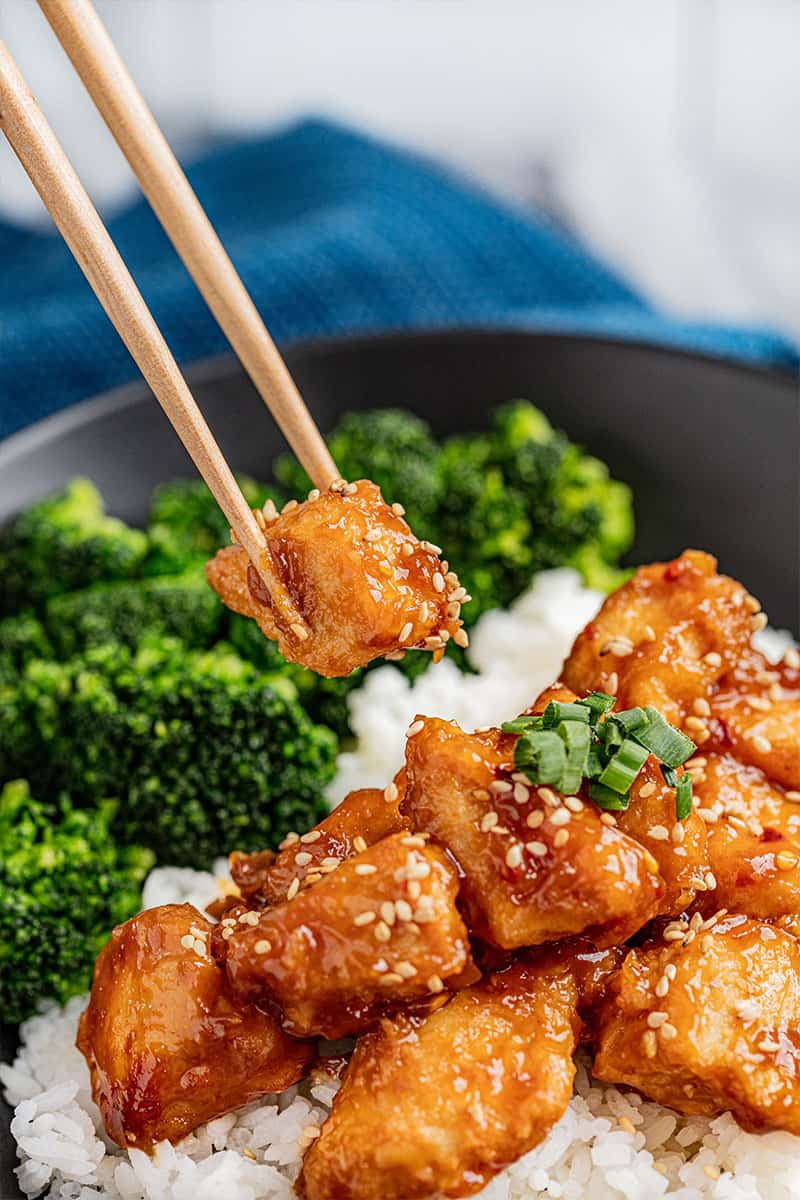 Chopsticks holding a piece of General Tso chicken.