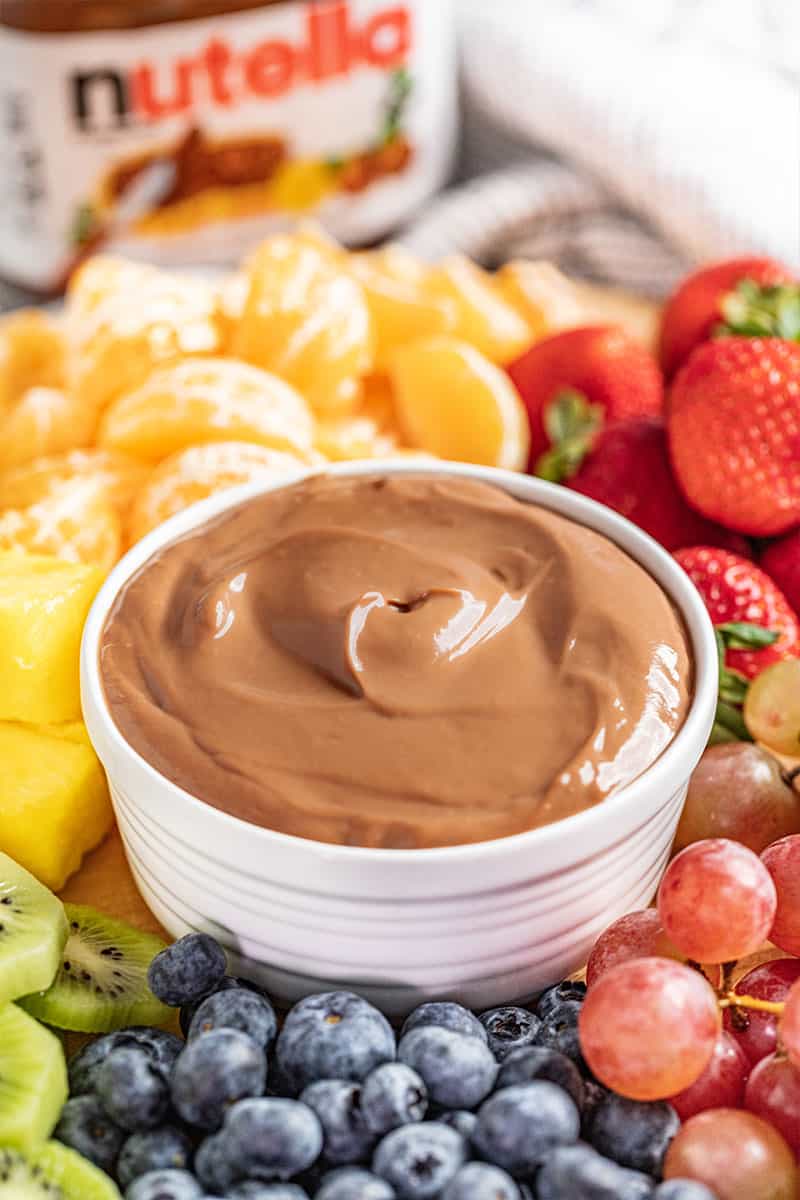 Nutella fruit dip surrounded by fruit with a jar of Nutella in the background.