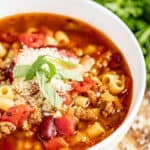 Pasta e fagioli in a soup bowl with freshly grated parmesan cheese and basil on top.