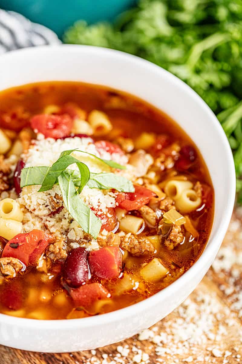 Pasta e fagioli in a soup bowl with freshly grated parmesan cheese and basil on top.
