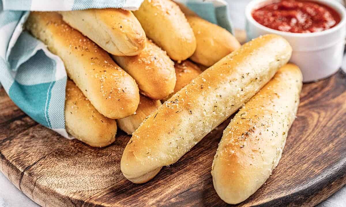 Breadsticks wrapped in a blue towel with marinara sauce in a bowl on the side.