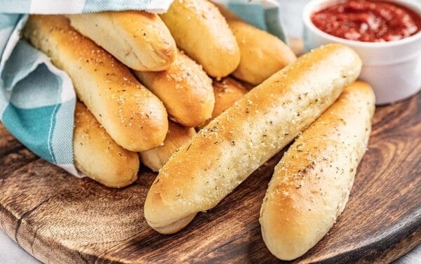 Breadsticks wrapped in a blue towel with marinara sauce in a bowl on the side.