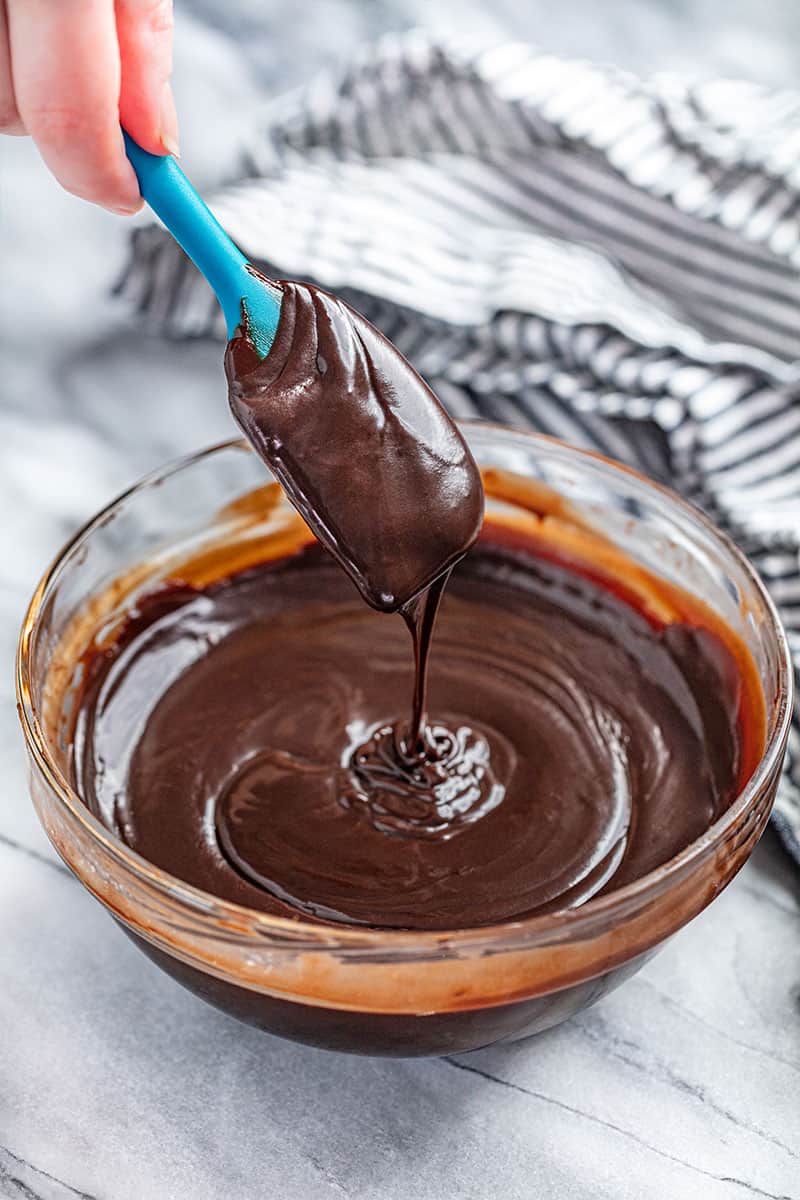 A spatula covered in chocolate ganache dripping into a bowl filled with chocolate ganache.