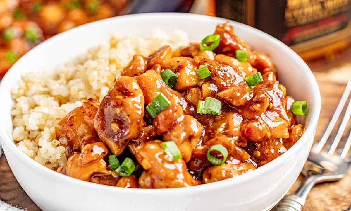 A white bowl filled with saucy bourbon chicken and rice.