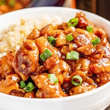 A white bowl filled with saucy bourbon chicken and rice.
