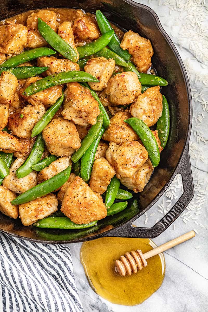 Overhead view of a skillet filled with sticky honey garlic chicken and snap peas.