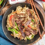 Beef lo mein in a bowl with a take out box nearby.