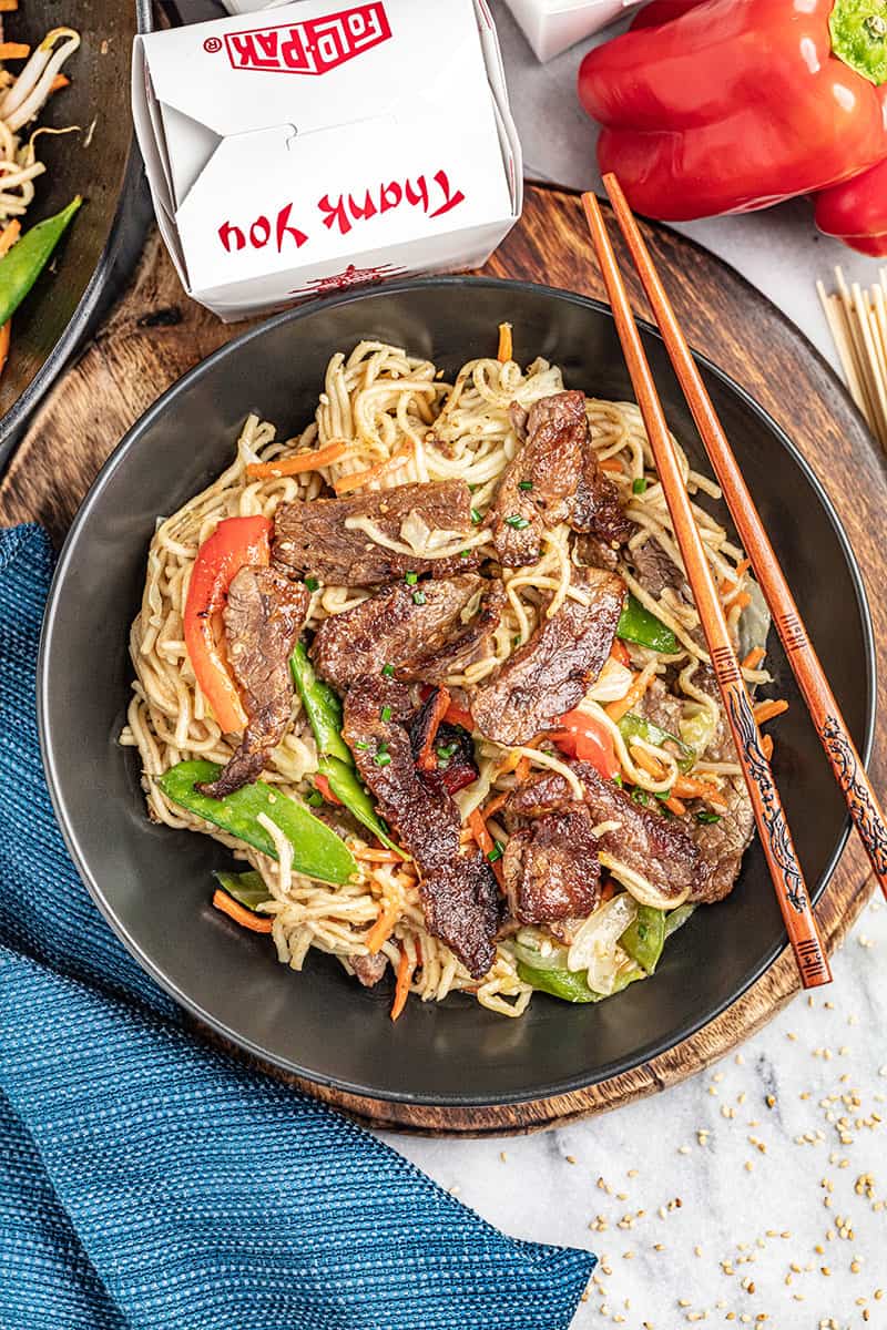 Beef lo mein in a bowl with a take out box nearby.