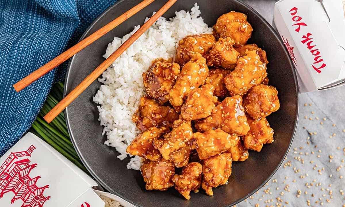 Overhead view of a bowl of white rice with takeout sesame chicken.